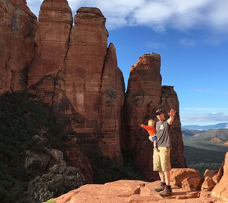 Person holding a baby hiking in a rocky region.
